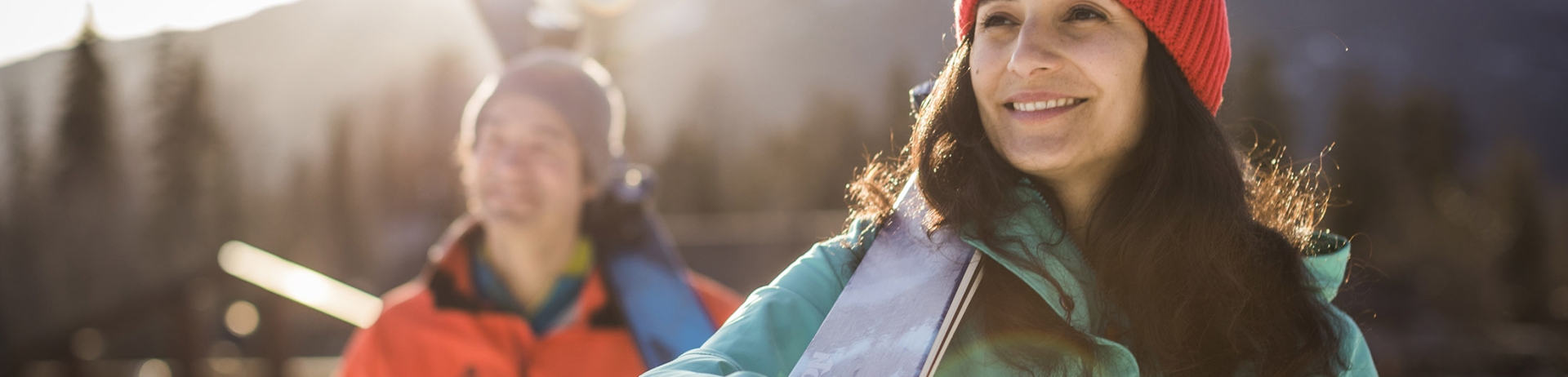 A man and woman carry their skis on their shoulders