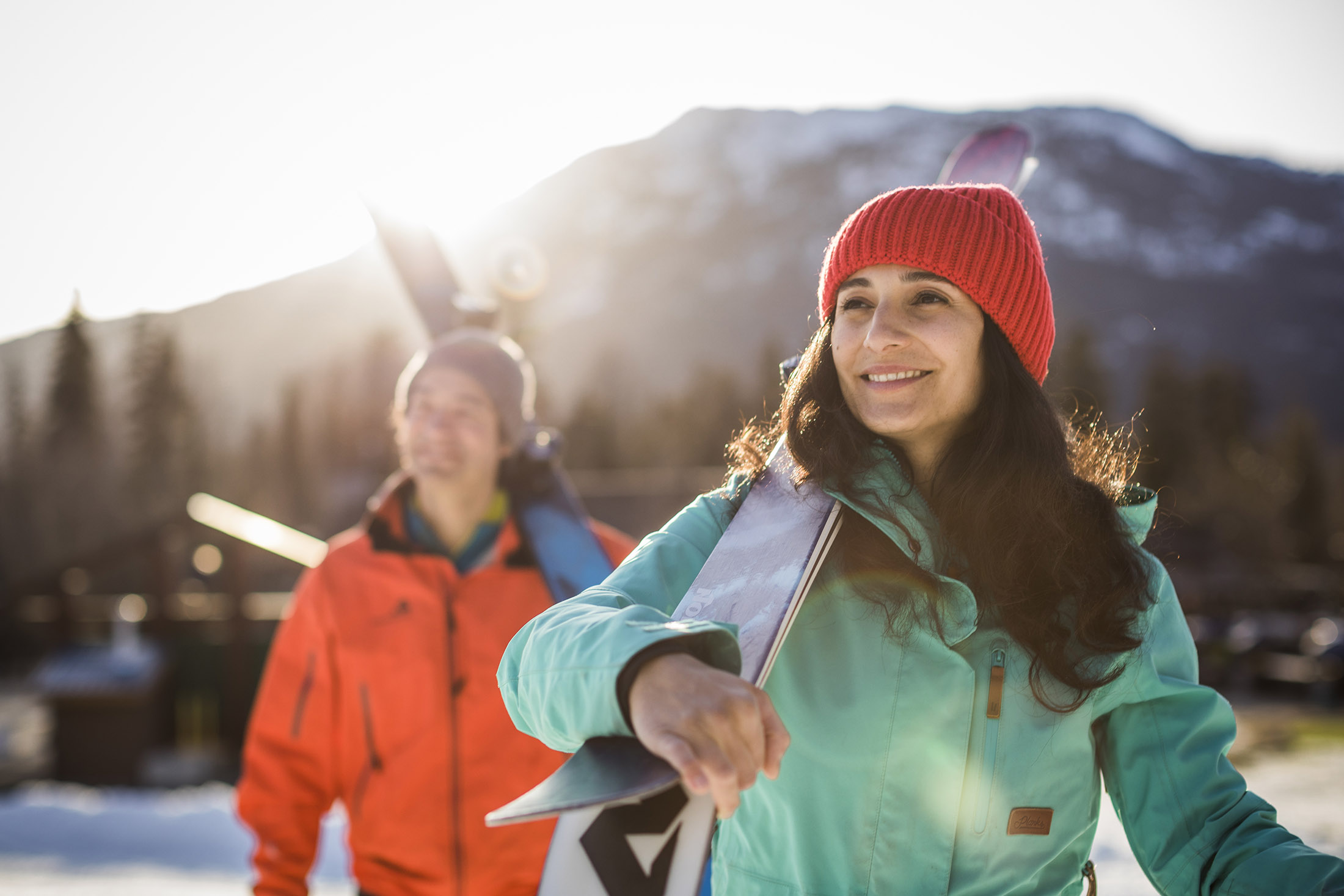 A man and woman carry their skis on their shoulders