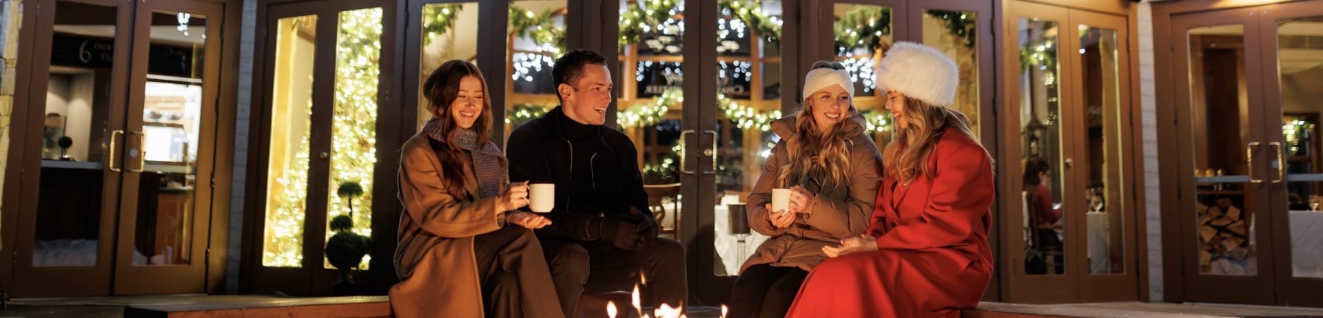 friends fireside enjoying a warm beverage with twinkling lights as a background at the chalet at fairmont chateau whistler