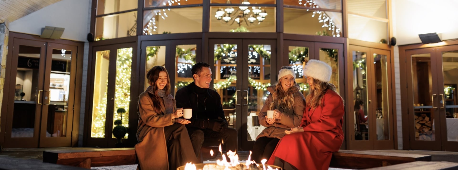 friends fireside enjoying a warm beverage with twinkling lights as a background at the chalet at fairmont chateau whistler