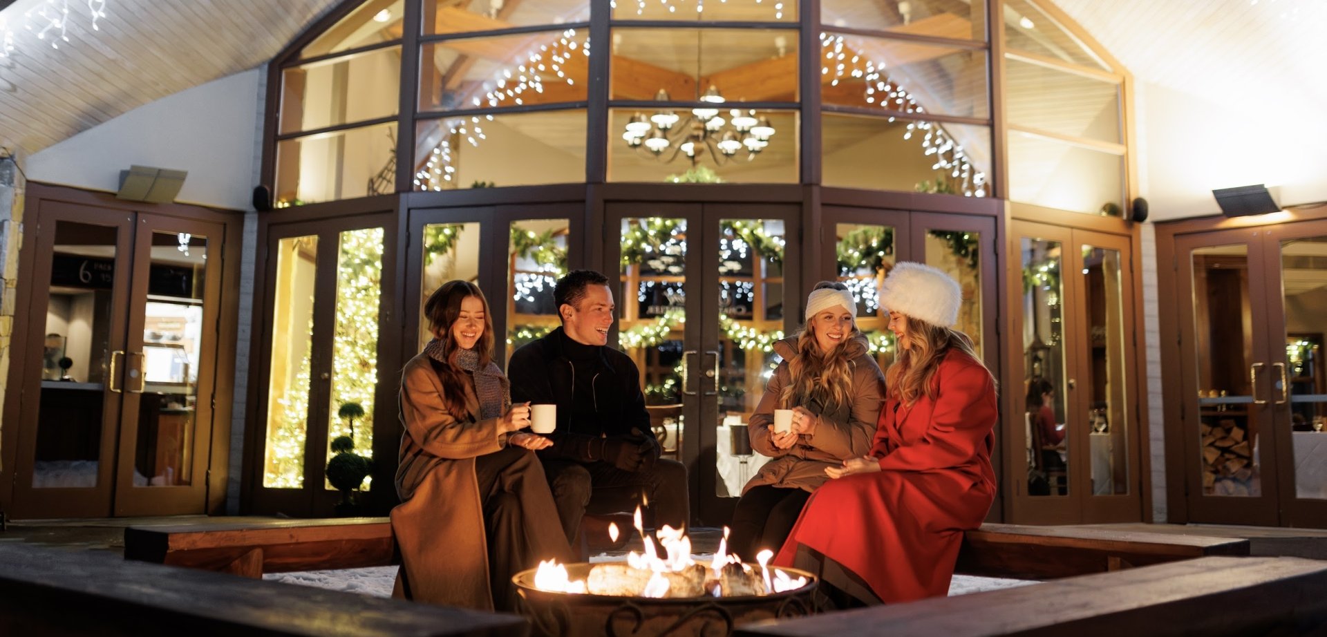 friends fireside enjoying a warm beverage with twinkling lights as a background at the chalet at fairmont chateau whistler