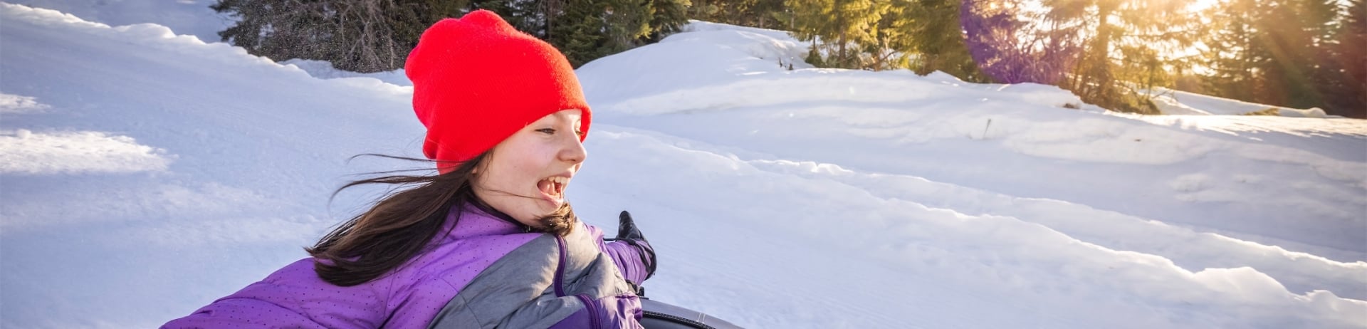 little girl in a purple snowsuit tubbing down a snowy hill