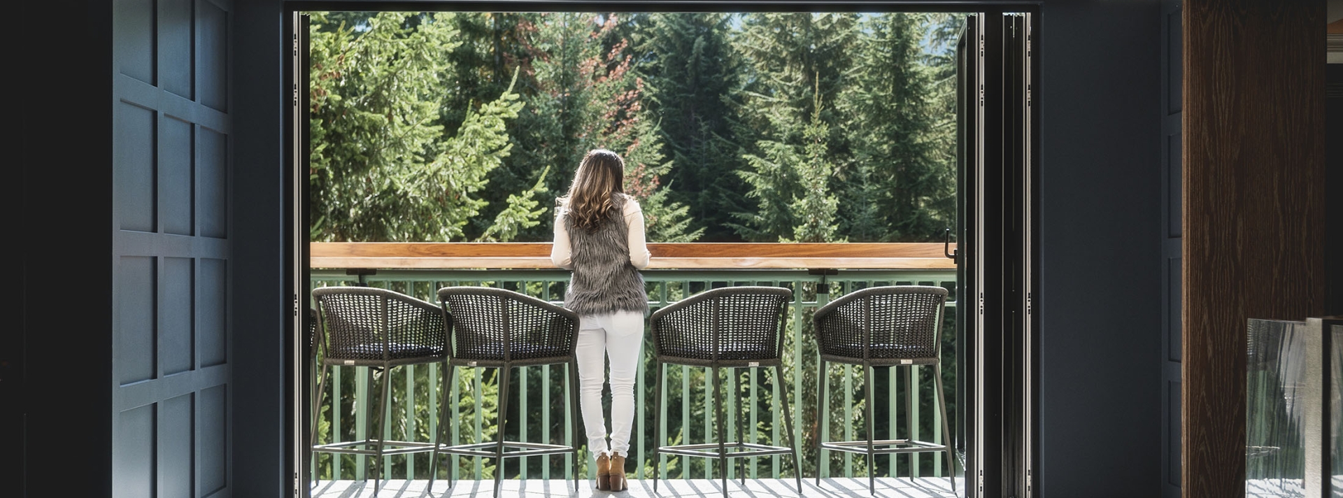 A woman stands on a patio overlooking trees