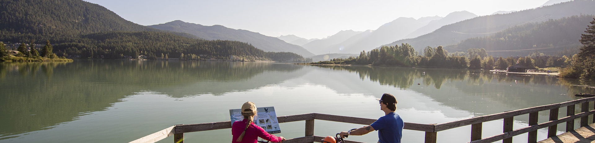 Two cyclists stop to look over the lake on a boardwalk