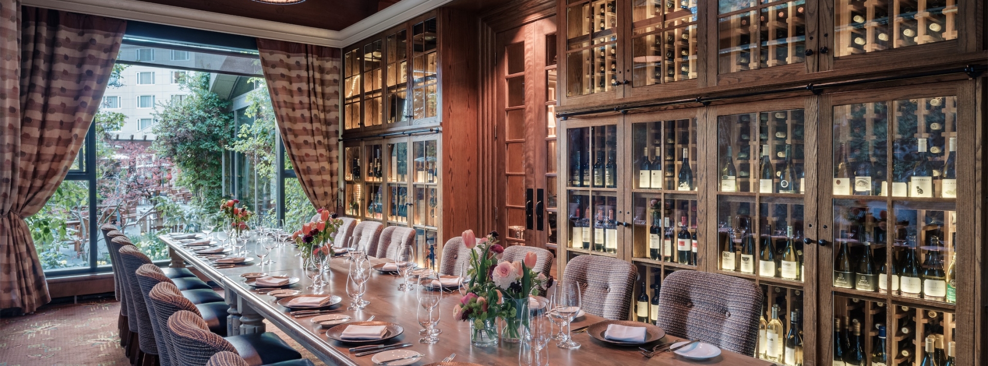 long table set for dinner with wall cabinets of wine in the background