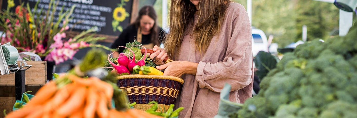 A woman shops for groceries, filling a basket with fresh vegetables