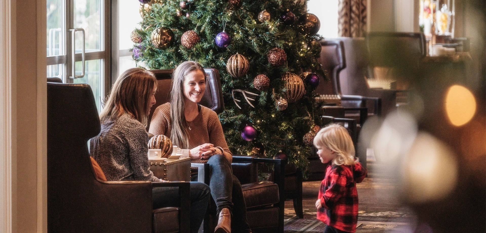 a little girl walking towards her mom and grandmother with a large christmas tree in the background
