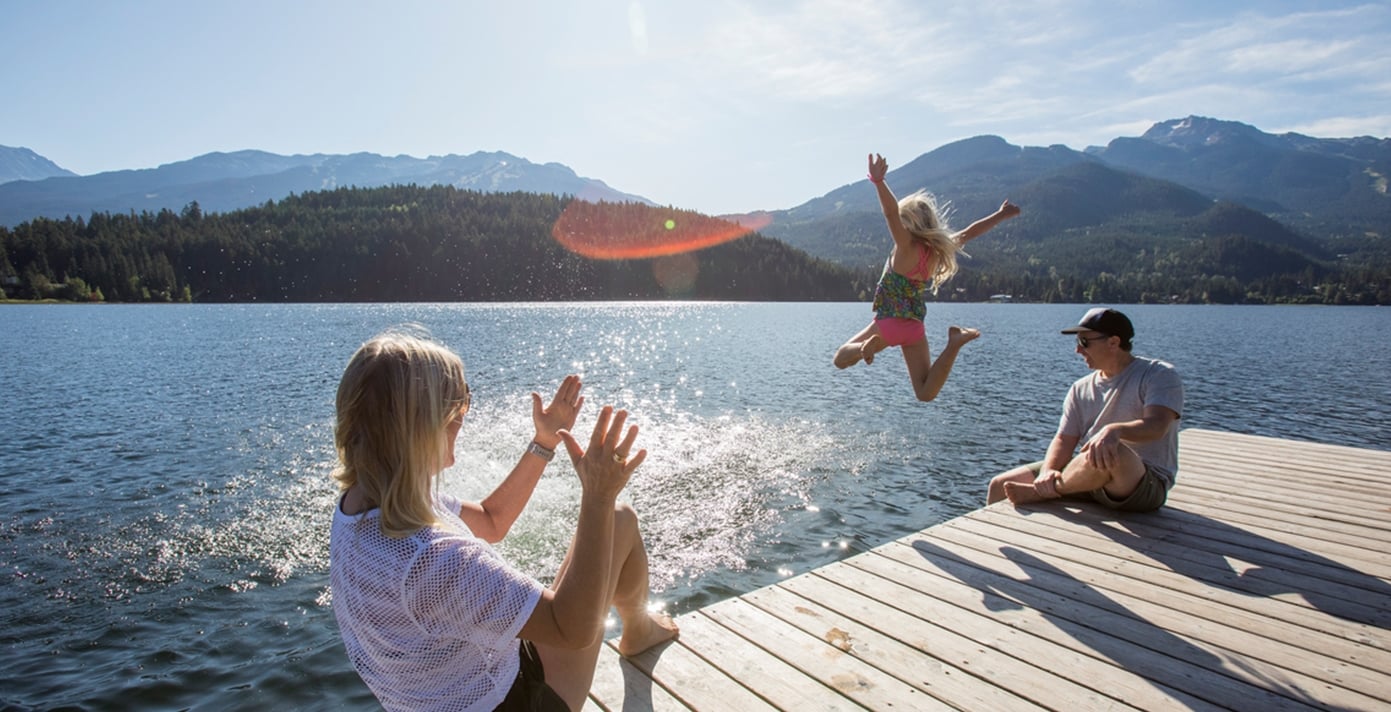 A child in swimwear jumps off a pier into a lake as her parents sit and watch