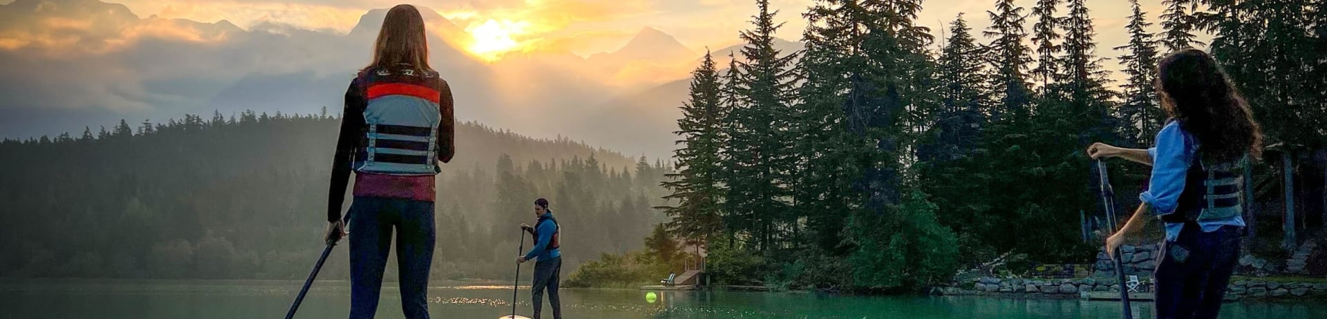 person on a paddle board on a body of water with trees in the background during sunset 