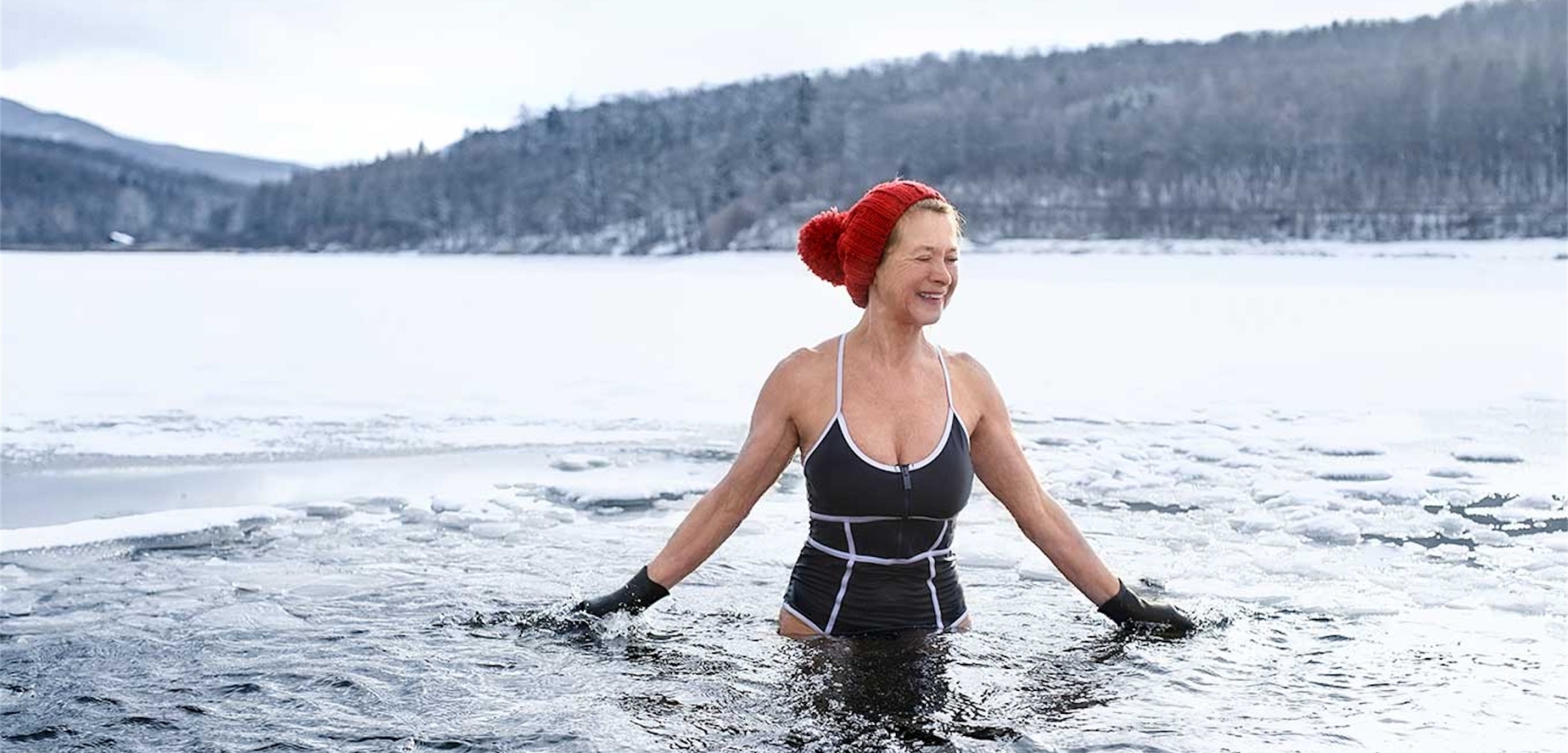 woman in bathing suit and red winter hat stands in a large body of water