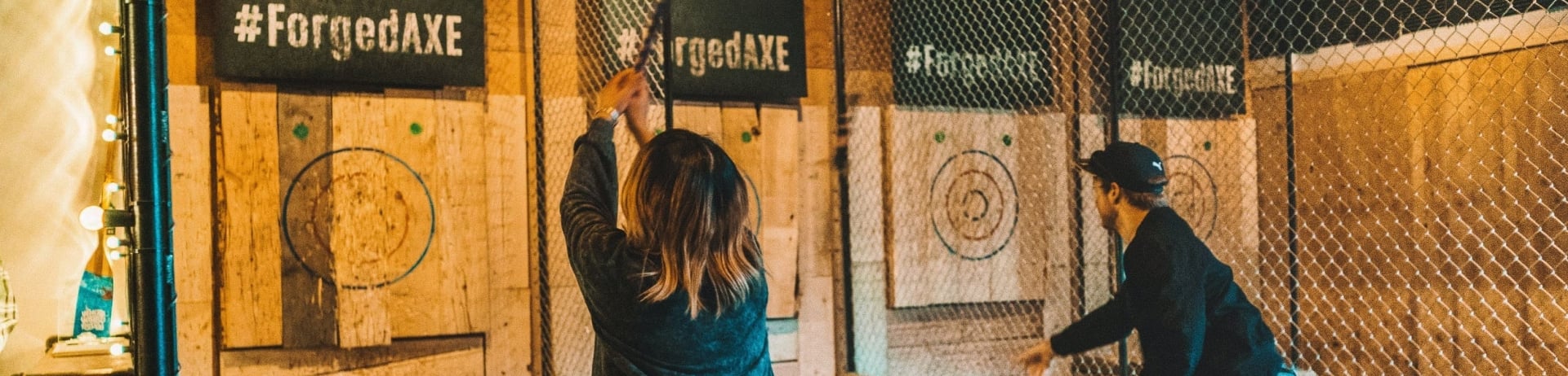 people throw axes toward a bullseye on a wall 