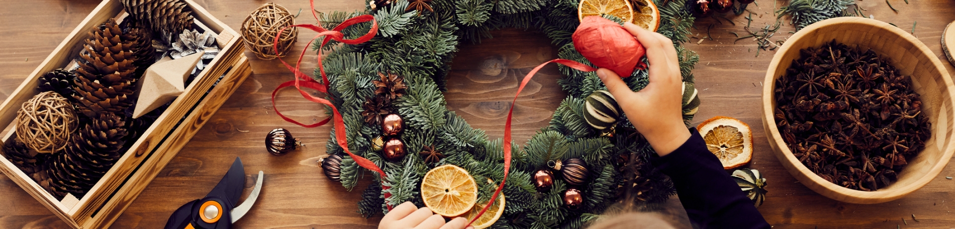 High angle view of busy woman standing at desk and using decorative ribbon while making Christmas wreath