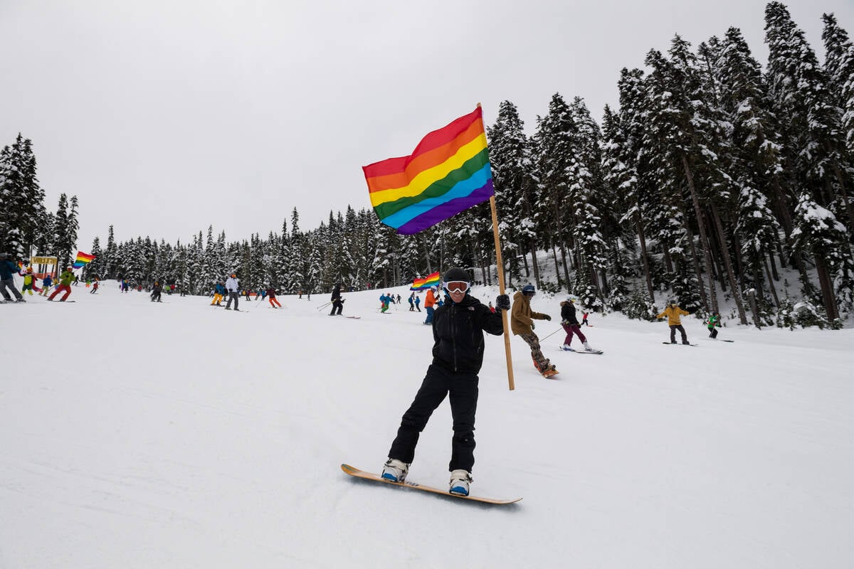 Snowboarder waving pride flag while going down the hill.