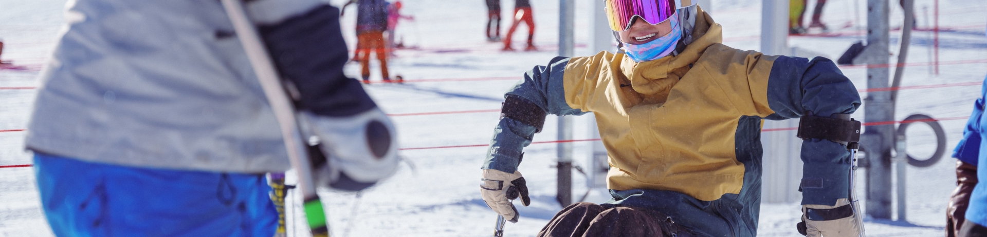 An adaptive athlete who is using a sit-ski smiles while talking with a friend while on a weekend winter ski trip to whistler
