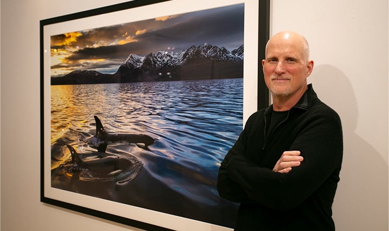 Paul Nicklen standing in front of his image of two orcas swimming