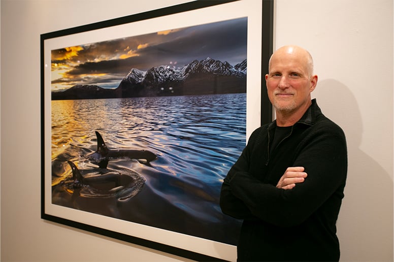 Paul Nicklen standing in front of his image of two orcas swimming