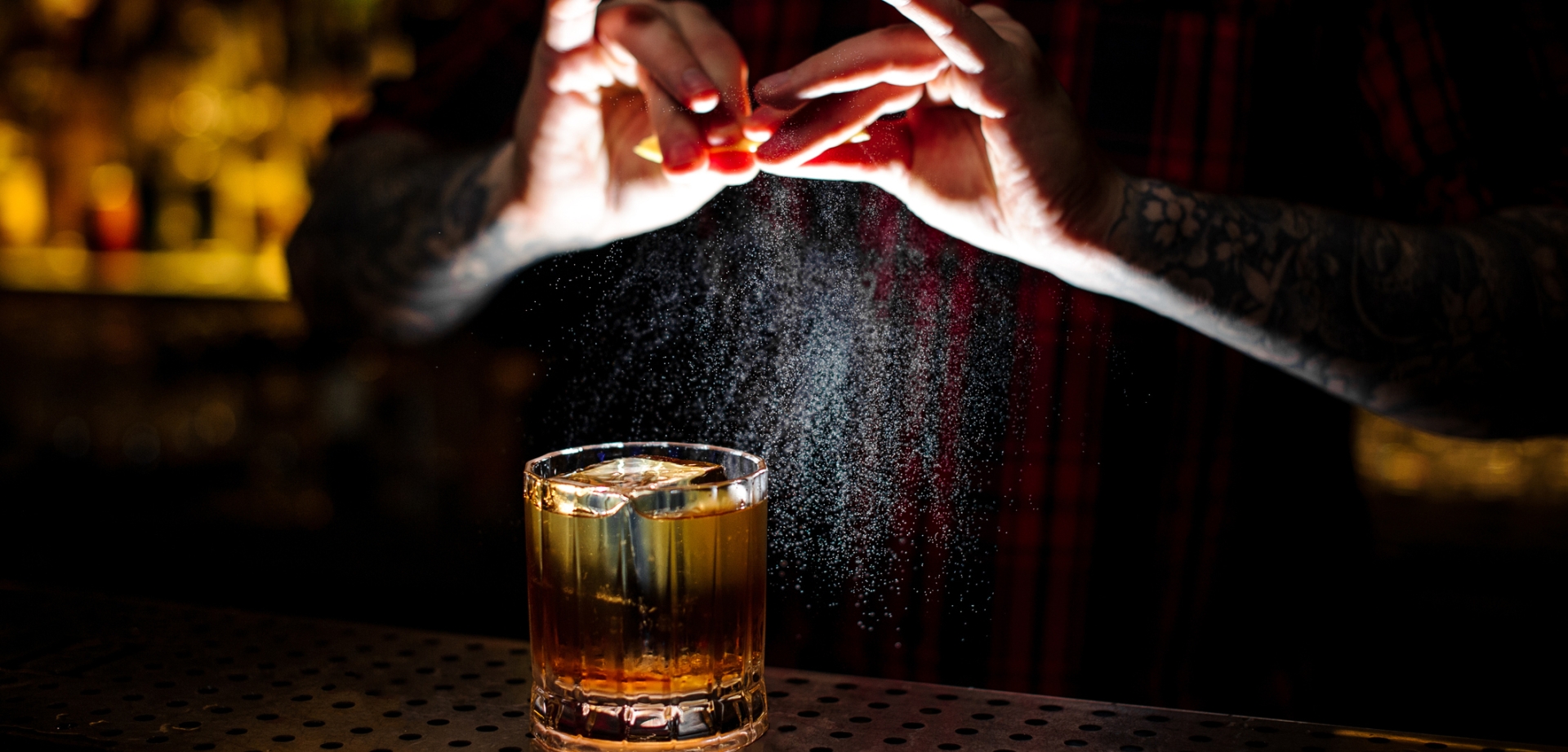 Barman splashing orange peel juice into a strong cocktail magic of scotch mixology class