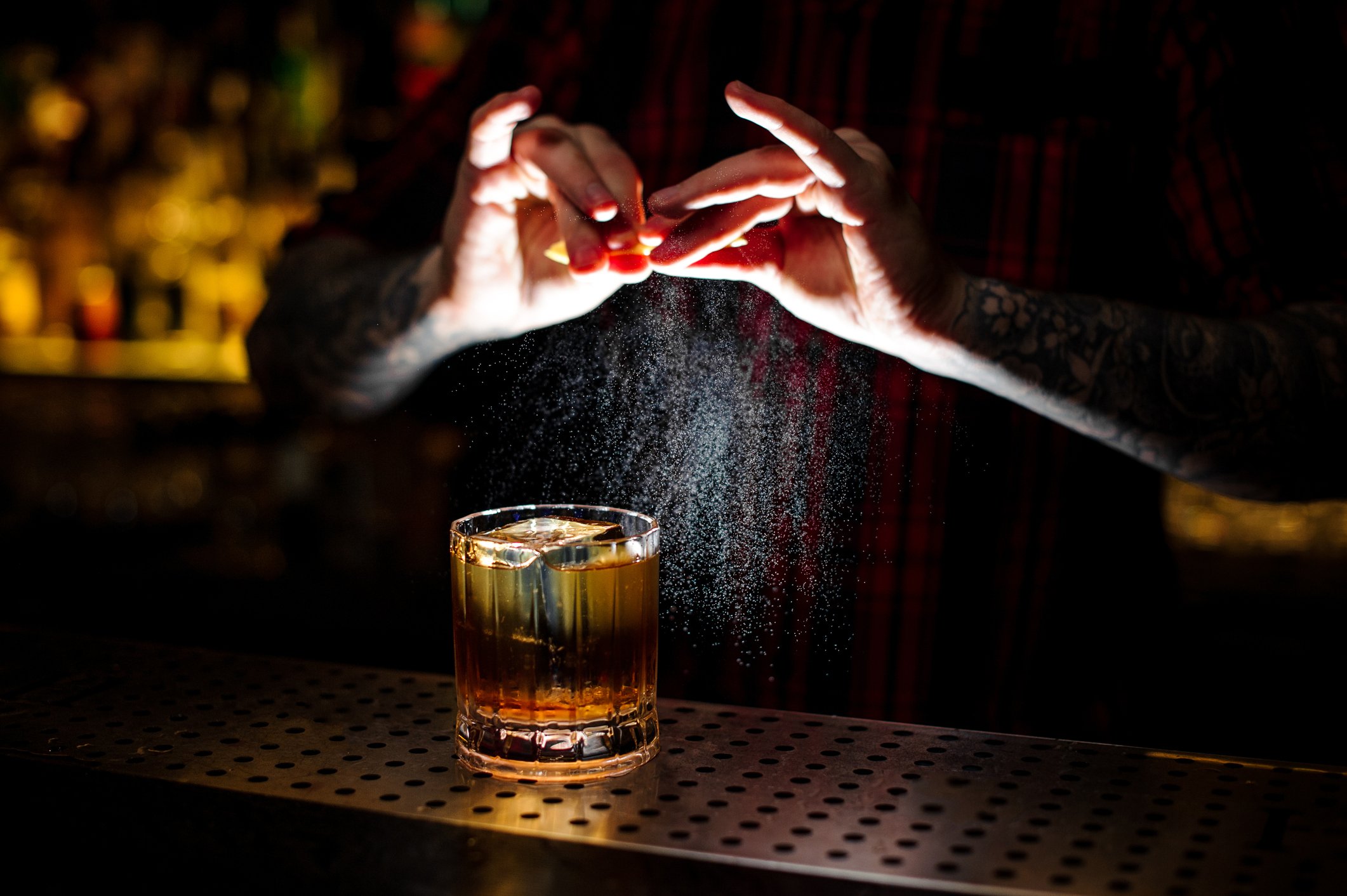 Barman splashing orange peel juice into a strong cocktail magic of scotch mixology class