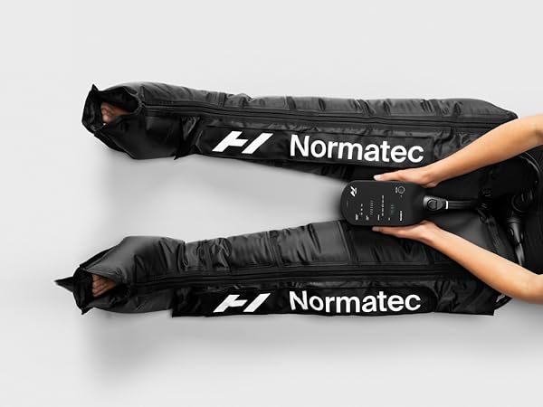 hyperice normatec boots with a person wearing them and sitting on the floor holding remote.