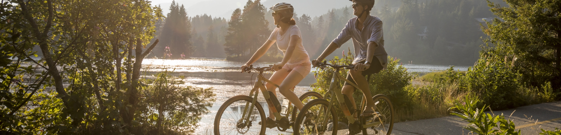 two people biking on a paved trail next to a lake in a mountain landscape