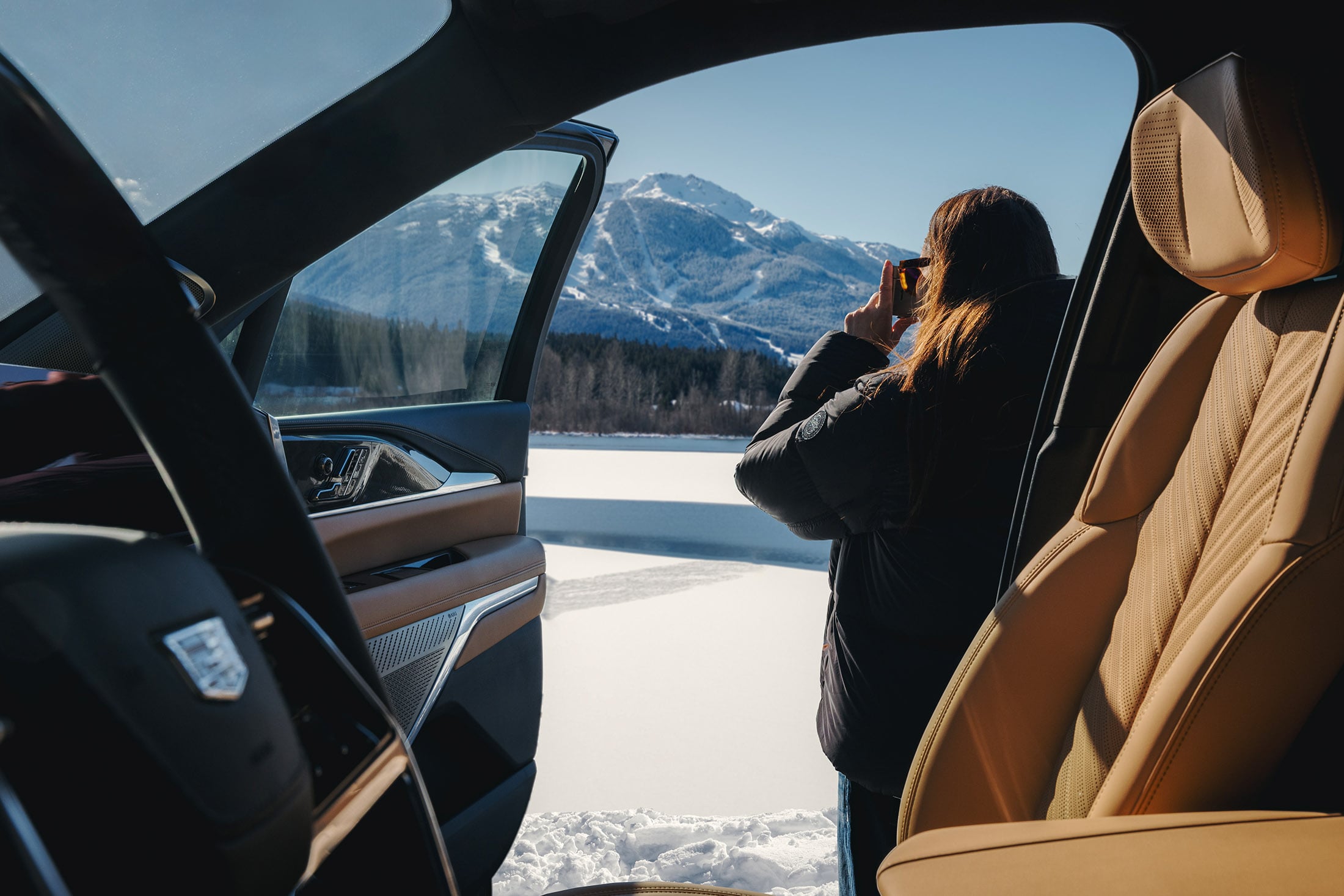 Guest photographing a snow-covered Whistler mountain landscape from inside a Cadillac luxury SUV with tan leather interior