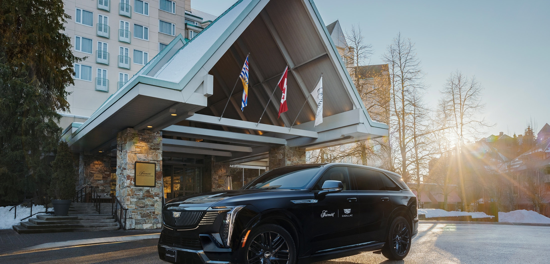 Branded Cadillac luxury SUV parked at the entrance of Fairmont Chateau Whistler at golden hour with BC and Canadian flags