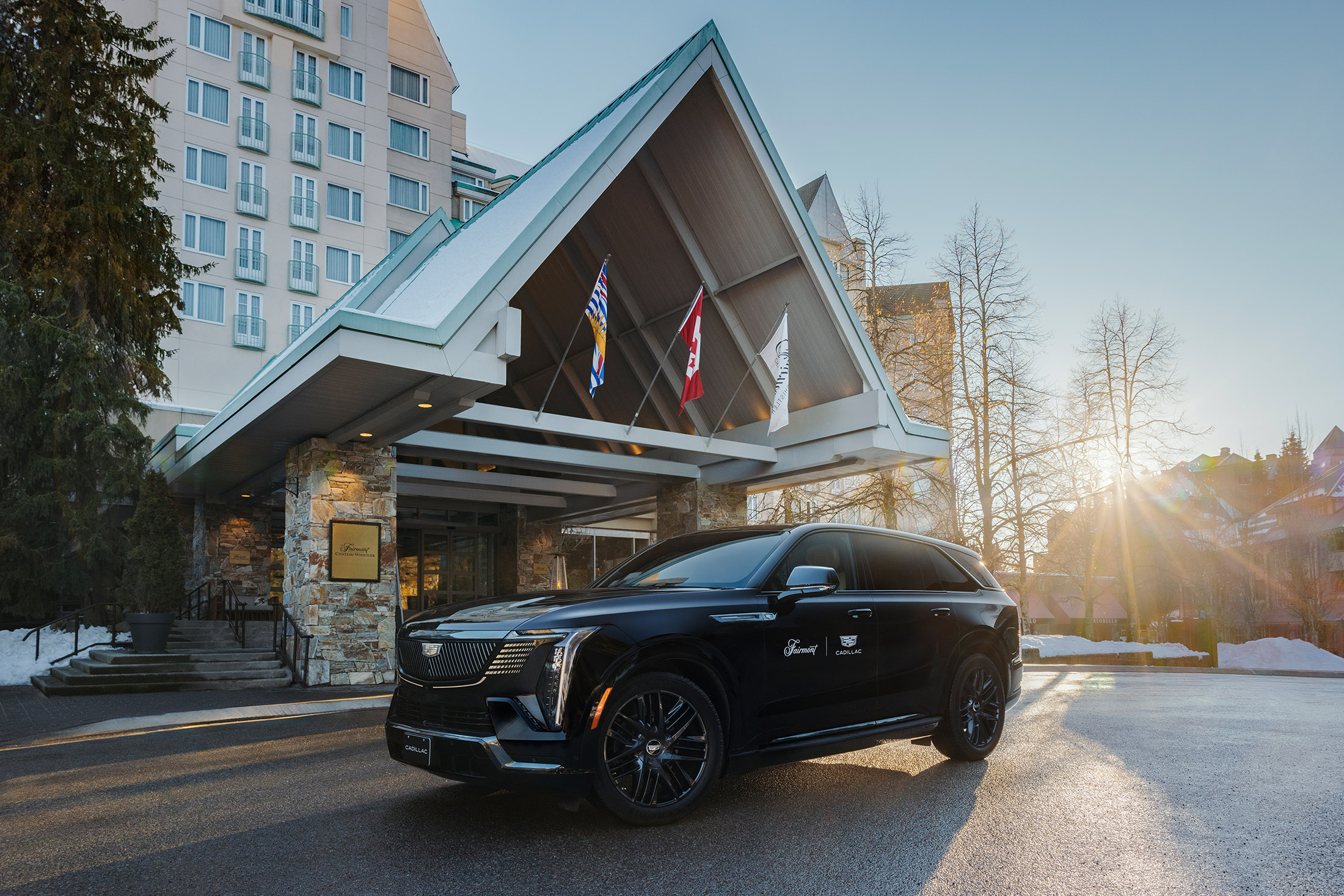 Branded Cadillac luxury SUV parked at the entrance of Fairmont Chateau Whistler at golden hour with BC and Canadian flags
