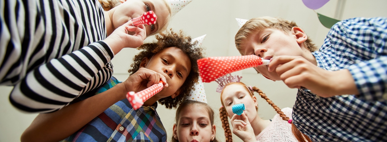 Low angle view at group of happy kids blowing party horns at camera and having fun