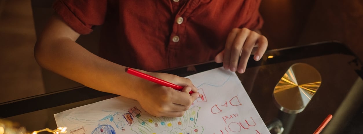 Child drawing Christmas tree and snowman for his mother and father
