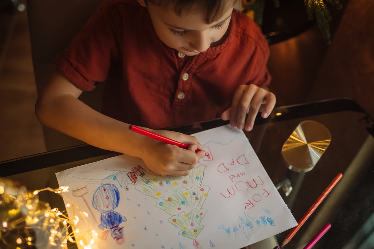 Child drawing Christmas tree and snowman for his mother and father
