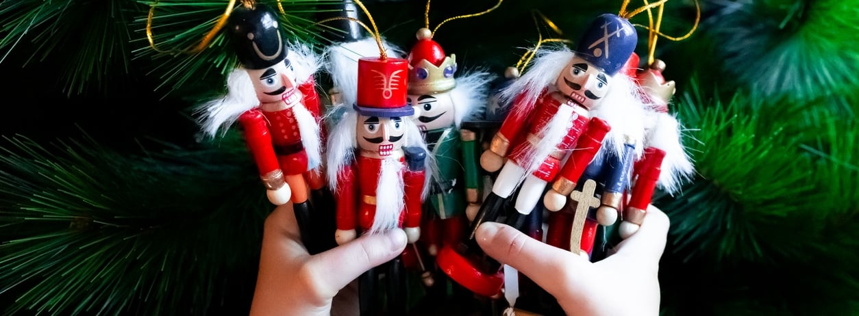 Child holding colorful wooden nutcracker ornaments against Christmas tree. High quality.