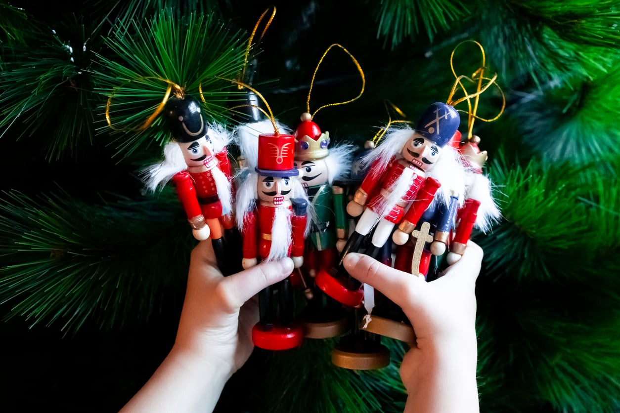 Child holding colorful wooden nutcracker ornaments against Christmas tree. High quality.