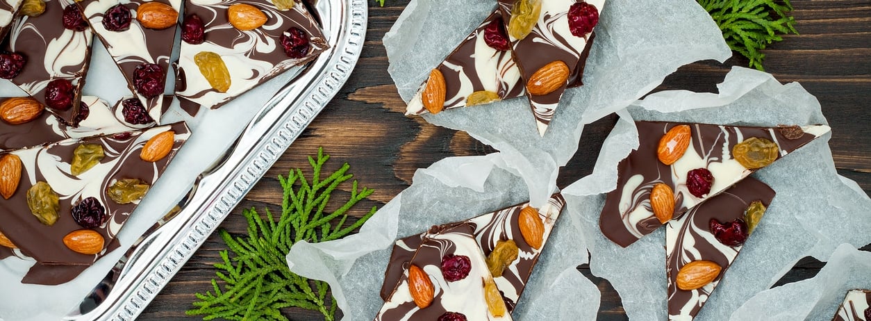 Holiday chocolate bark with dried fruits and nuts on a dark wood background. Top view.