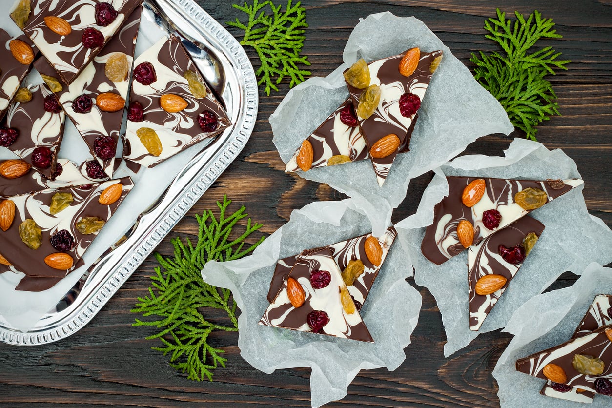Holiday chocolate bark with dried fruits and nuts on a dark wood background. Top view.
