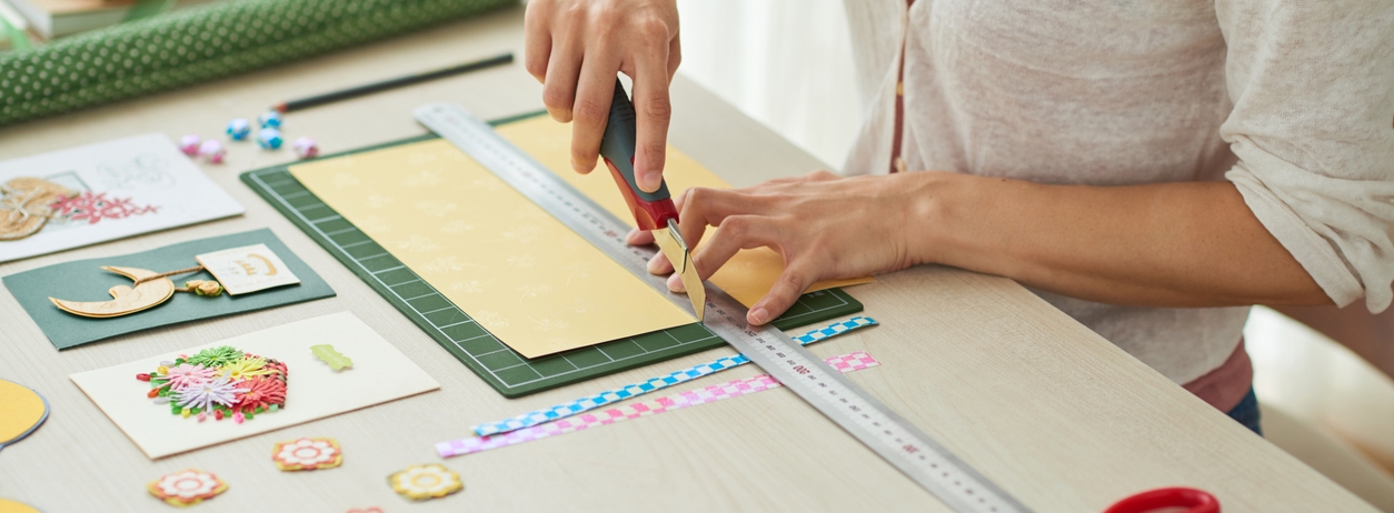 Creative woman sitting at wooden table and making greeting cards for her friends, scrapbooking items lying on surface